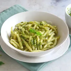 Un piatto invitante di pasta al pesto, condita con basilico fresco e pinoli. Accanto, un mortaio con altro pesto fatto in casa.