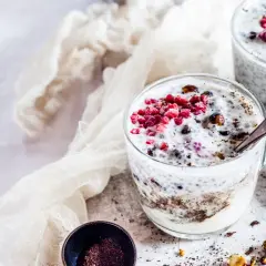 Due bicchieri di yogurt con semi di chia, lamponi e granella di nocciole. Un dessert sano e gustoso.