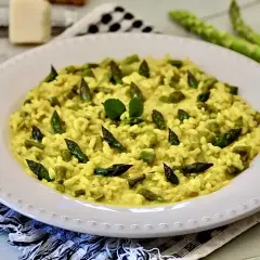 Un cremoso risotto con asparagi, guarnito con punte di asparagi freschi e una fogliolina verde.