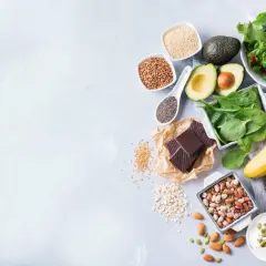 Banane, spinaci, avocado, cioccolato fondente e altri 20 alimenti che alzano la pressione, disposti su un piano grigio.