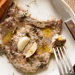 Braciole di maiale succulente, condite con aglio e erbe aromatiche, pronte per essere gustate con pane croccante.