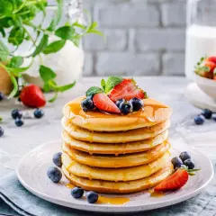 Pila di soffici pancake senza glutine, guarniti con fragole, mirtilli e sciroppo d'acero.