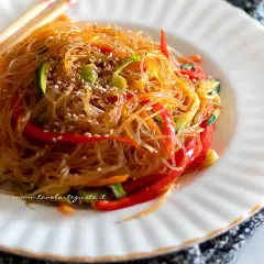Un piatto invitante di spaghetti di soia con verdure colorate, peperoni rossi, zucchine e carote, guarnito con semi di sesamo.