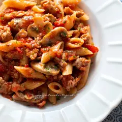 Piatto di pasta alla boscaiola con penne, funghi, salsiccia e pomodoro, condita con prezzemolo fresco.