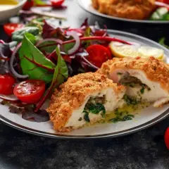 Pollo alla Kiev croccante, ripieno di spinaci e burro, servito con un'insalata fresca di pomodorini e cipolla rossa.