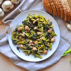 Un piatto di salsiccia e rape saltate, con pane integrale, aglio e cipollotti freschi.