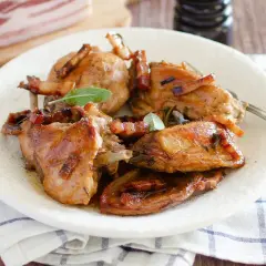 Delizioso coniglio in padella, dorato e succulento, guarnito con pancetta croccante e foglie di salvia fresca.