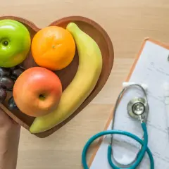 Frutta fresca in un vassoio a forma di cuore, accanto a uno stetoscopio e un glucometro, per capire come abbassare la glicemia con una dieta sana.