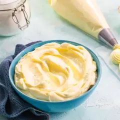 Una ciotola blu piena di soffice crema al mascarpone, pronta per decorare dolci. Accanto, sac à poche e uova.