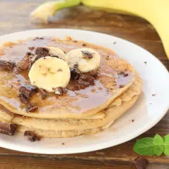 Pancake alla banana con scaglie di cioccolato e sciroppo d'acero, guarniti con fettine di banana fresca.