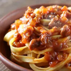 Tagliatelle al ragù, un classico dei primi piatti di carne, servite in una ciotola di terracotta.