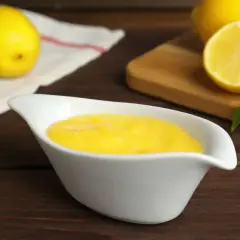 Una ciotola bianca contiene una deliziosa crema al limone, con limoni freschi sullo sfondo.