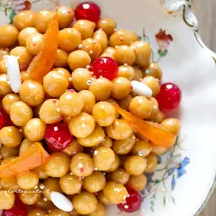 Struffoli ricetta napoletana: palline dorate glassate, ciliegie rosse, canditi e confettini in un piatto decorato.