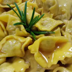 Un piatto invitante di ravioli del plin, conditi con un sugo dorato e guarniti con un rametto di rosmarino fresco.