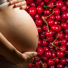 Pancia di donna incinta accarezzata, circondata da un mare di ciliegie rosse, simbolo di dolce attesa e ciliegie in gravidanza.