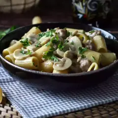 Piatto fumante di pasta con funghi e salsiccia, guarnito con prezzemolo fresco. Un classico confortante.