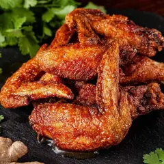 Alette di pollo dorate e succulente, servite su una pietra scura con coriandolo fresco, zenzero e aglio.