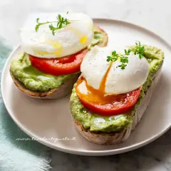 Due fette di pane tostato con avocado, pomodoro e un perfetto uovo in camicia, guarnito con germogli freschi.