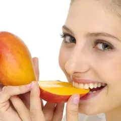 Ragazza sorridente morde un mango succoso, sapendo che il mango è lassativo.