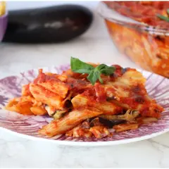Piatto di pasta alla siciliana con melanzane, pomodoro e formaggio fuso, guarnito con basilico fresco.