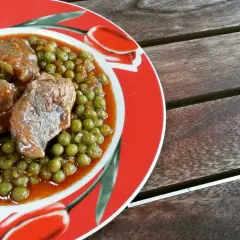 Un gustoso spezzatino con piselli, servito su un piatto rosso decorato con tulipani, pronto per essere gustato.