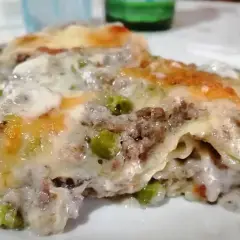 Porzione di lasagne bianche sfiziose con ragù, piselli e besciamella filante, gratinate al forno.