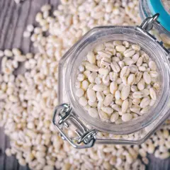 Orzo perlato in un barattolo di vetro, circondato da chicchi sparsi. Attenzione, l'orzo fa ingrassare se consumato in eccesso!