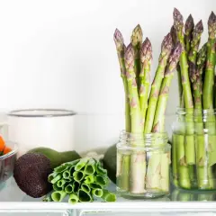 Asparagi freschi in barattoli con acqua, un ottimo modo per conservare gli asparagi. Vicino pomodorini, avocado e cipollotti.