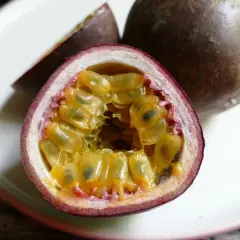 Un frutto della passione tagliato a metà, con la polpa succosa e i semi visibili, su un piatto bianco.