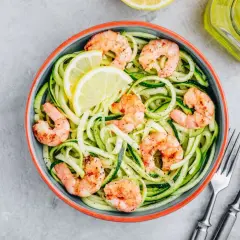 Piatto di spaghetti di zucchine con gamberetti saltati e spicchi di limone. Un modo semplice per imparare come cuocere i gamberetti surgelati.