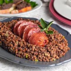 Piatto di lenticchie con fette di cotechino fresco, guarnito con una fogliolina di salvia.