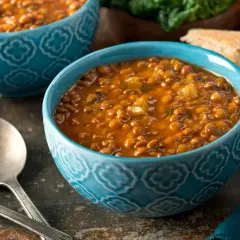 Due ciotole blu con un saporito stufato di riso e ceci, accompagnato da pane rustico e verdure fresche.