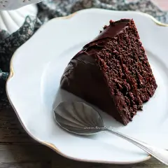 Una fetta di torta al cioccolato, ricca e umida, su un piatto bianco con un cucchiaino.