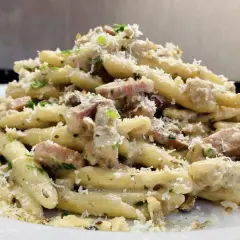 Un piatto invitante di pasta con speck, condita con una cremosa salsa, prezzemolo tritato e abbondante parmigiano grattugiato.