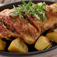 Succulento agnello al forno, dorato e profumato al rosmarino, servito con patate arrosto in una padella di ghisa.
