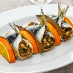 Sarde a beccafico su un piatto bianco, guarnite con fette d'arancia e foglie di alloro. Un piatto tradizionale siciliano.