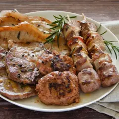 Un piatto ricco di **grigliata di carne**: costine, spiedini, salsicce e hamburger, guarniti con rosmarino fresco.