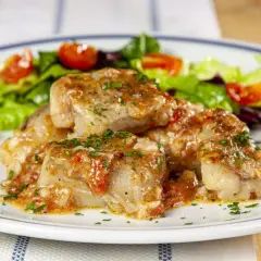 Deliziosi bocconcini di coda di rospo in umido con pomodoro e prezzemolo, accompagnati da insalata fresca e spicchi di limone.