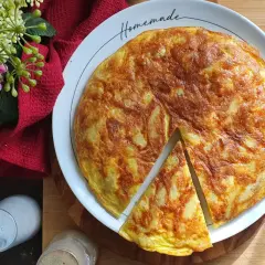 Una deliziosa frittata di patate fatta in casa, dorata e invitante, servita su un piatto bianco con fiori rosa e un tovagliolo rosso.