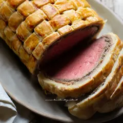 Un succulento filetto alla Wellington, cotto alla perfezione e avvolto in pasta sfoglia dorata, pronto per essere gustato.