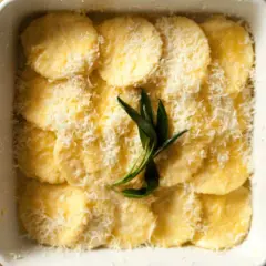 Gnocchi alla Romana pronti per essere infornati, conditi con parmigiano grattugiato e un rametto di salvia.