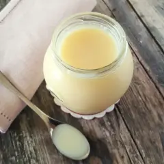 Un vasetto di latte condensato fatto in casa, denso e cremoso, pronto per dolci deliziosi. Un cucchiaino ne mostra la consistenza perfetta.
