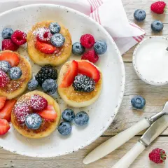 Deliziosi pancake senza glutine guarniti con fragole, lamponi, mirtilli e more. Serviti con yogurt e spolverata di zucchero a velo.