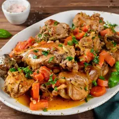 Un saporito coniglio in umido con carote e erbe aromatiche, servito su un piatto bianco.