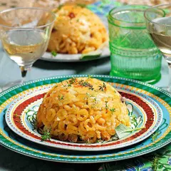 Anelletti al forno dorati e invitanti, guarniti con erbe aromatiche, serviti su piatti colorati con bicchieri di vino bianco.