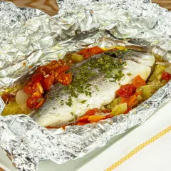 Orata al cartoccio con pomodorini e verdure, cotta al forno in un involucro di alluminio, pronta per essere gustata.