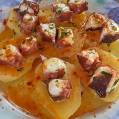 Un delizioso polpo alla gallega su patate, condito con paprika e prezzemolo, servito su un piatto blu e bianco.