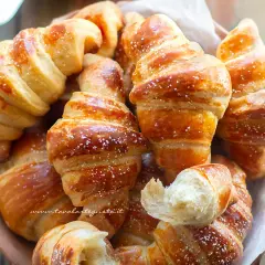 Cornetti fatti in casa dorati e soffici, spolverati di zucchero a velo, invitano a una colazione golosa.