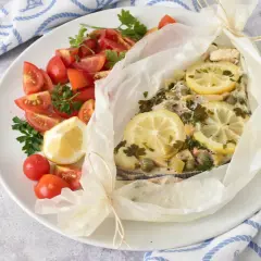 Delizioso pesce spada al forno in cartoccio con limone, capperi e prezzemolo, accompagnato da pomodorini freschi.