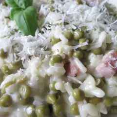 Un cremoso riso con piselli, guarnito con parmigiano grattugiato e un rametto di basilico. Un piatto che sa di casa.